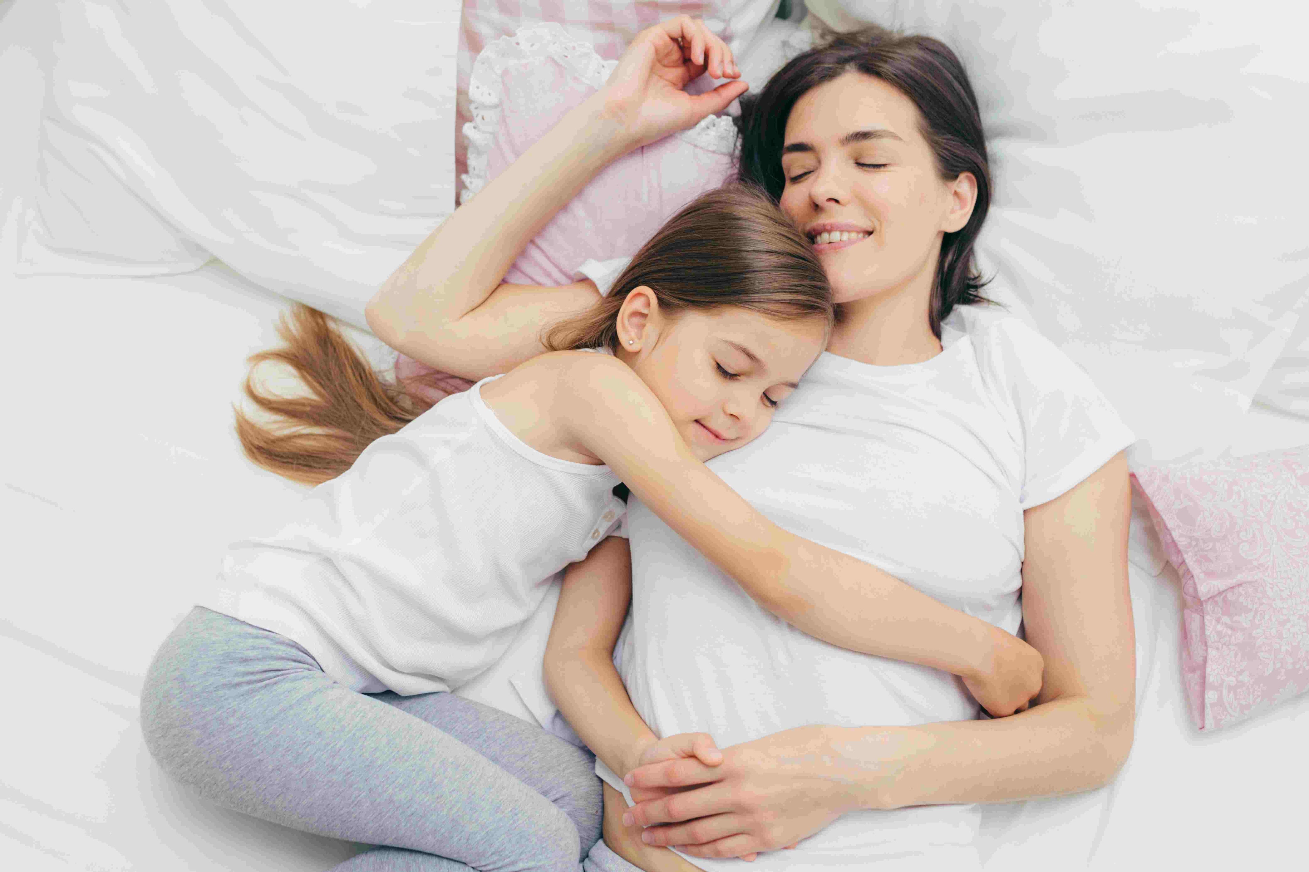 Waarom slaap zo belangrijk is voor je gezondheid: een moeder en dochter die samen ontspannen in bed liggen.